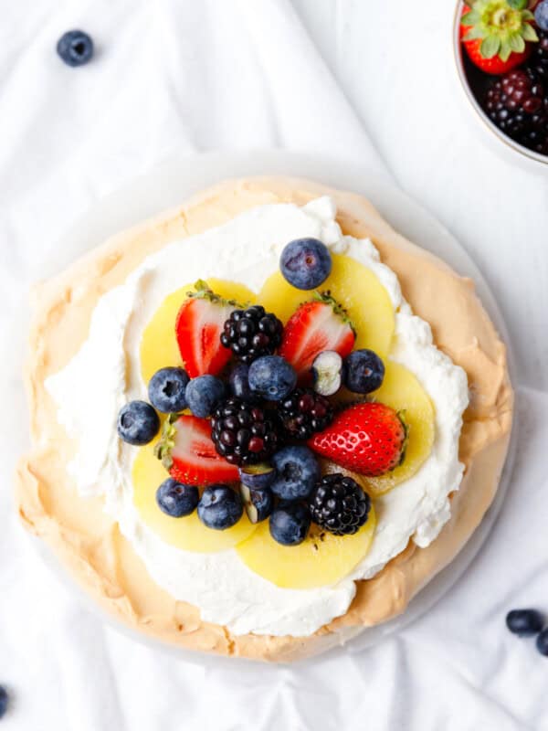 Keto pavlova overhead shot — meringue shell topped with whipped cream, kiwi slices, strawberries, blueberries, and blackberries on a white surface
