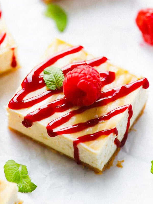 Keto raspberry cheesecake bar with almond flour crust, drizzled with raspberry sauce and topped with a fresh raspberry and mint