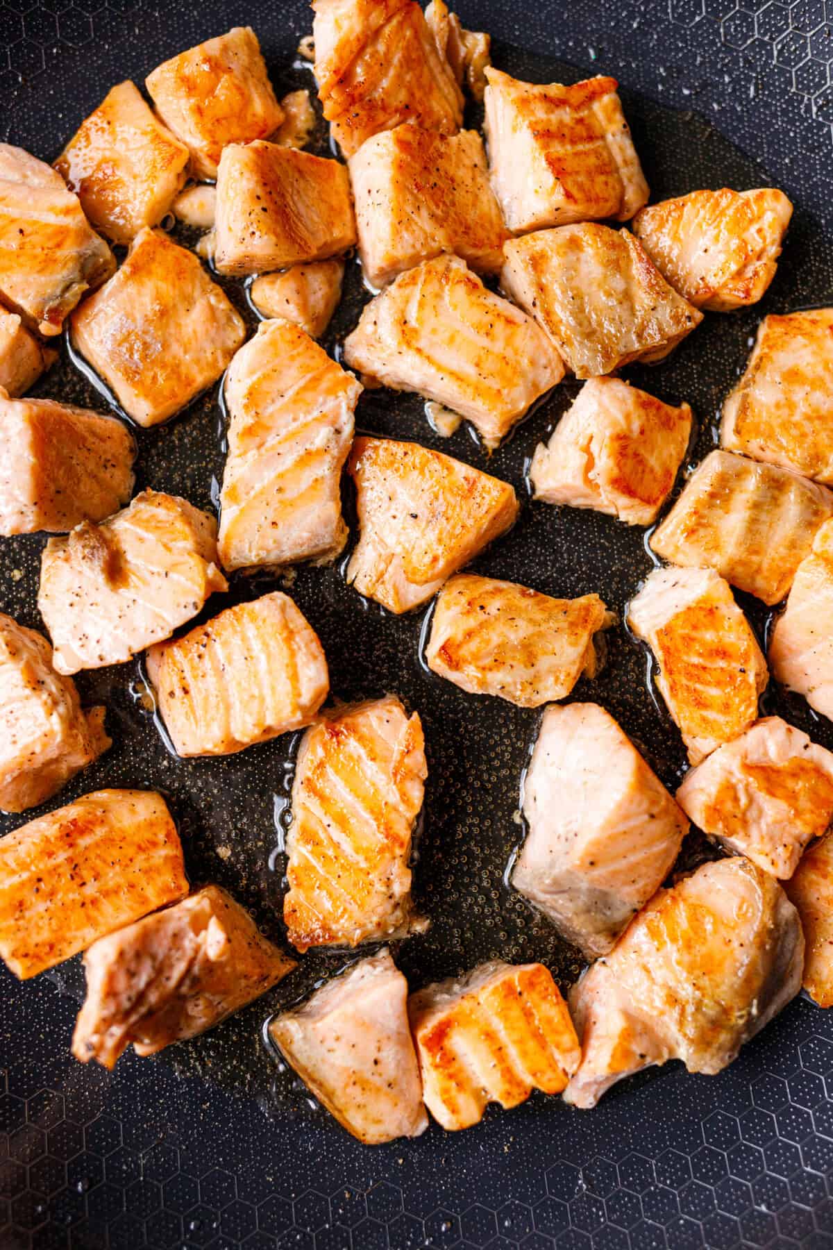Cubes of salmon seared golden brown in a nonstick skillet for a cooked salmon poke bowl
