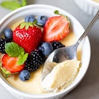 Spoon lifting a creamy bite of baked keto custard topped with strawberries, blueberries, blackberries and mint