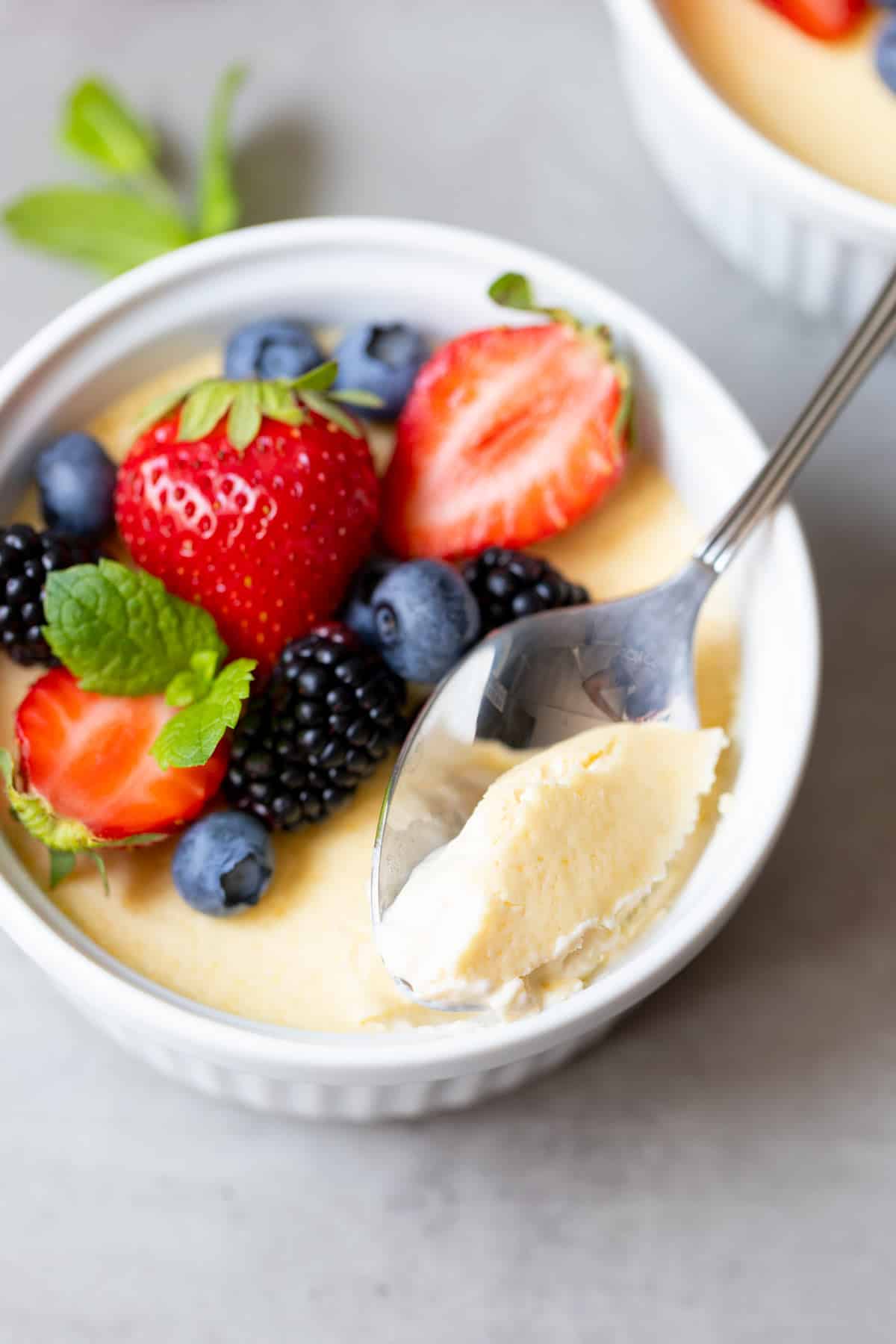 Spoon lifting a creamy bite of baked keto custard topped with strawberries, blueberries, blackberries and mint
