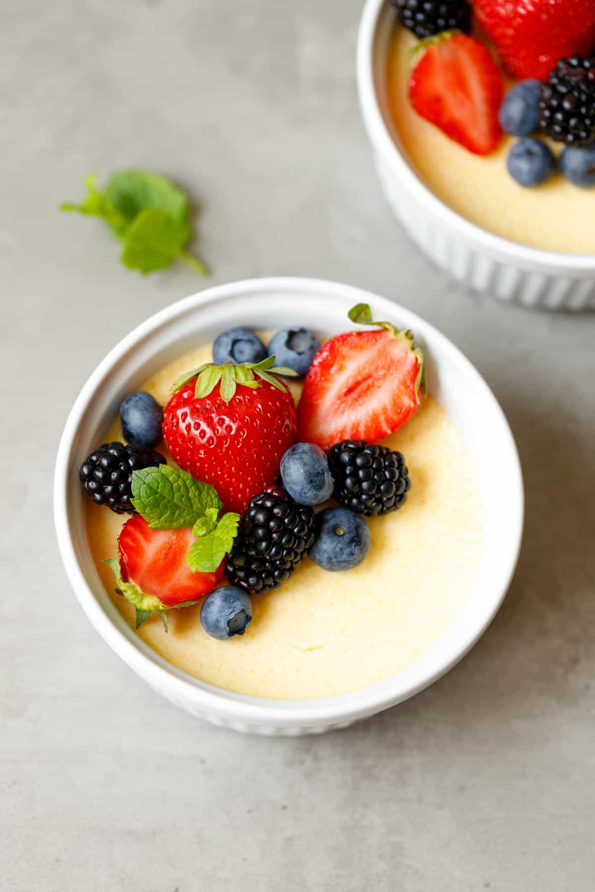 Two white ramekins of sugar-free low carb custard topped with mixed berries and a sprig of mint