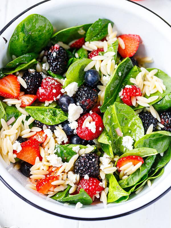 Overhead view of berry spinach orzo salad with strawberries, blueberries, blackberries, raspberries, feta crumbles, and orzo in a white bowl