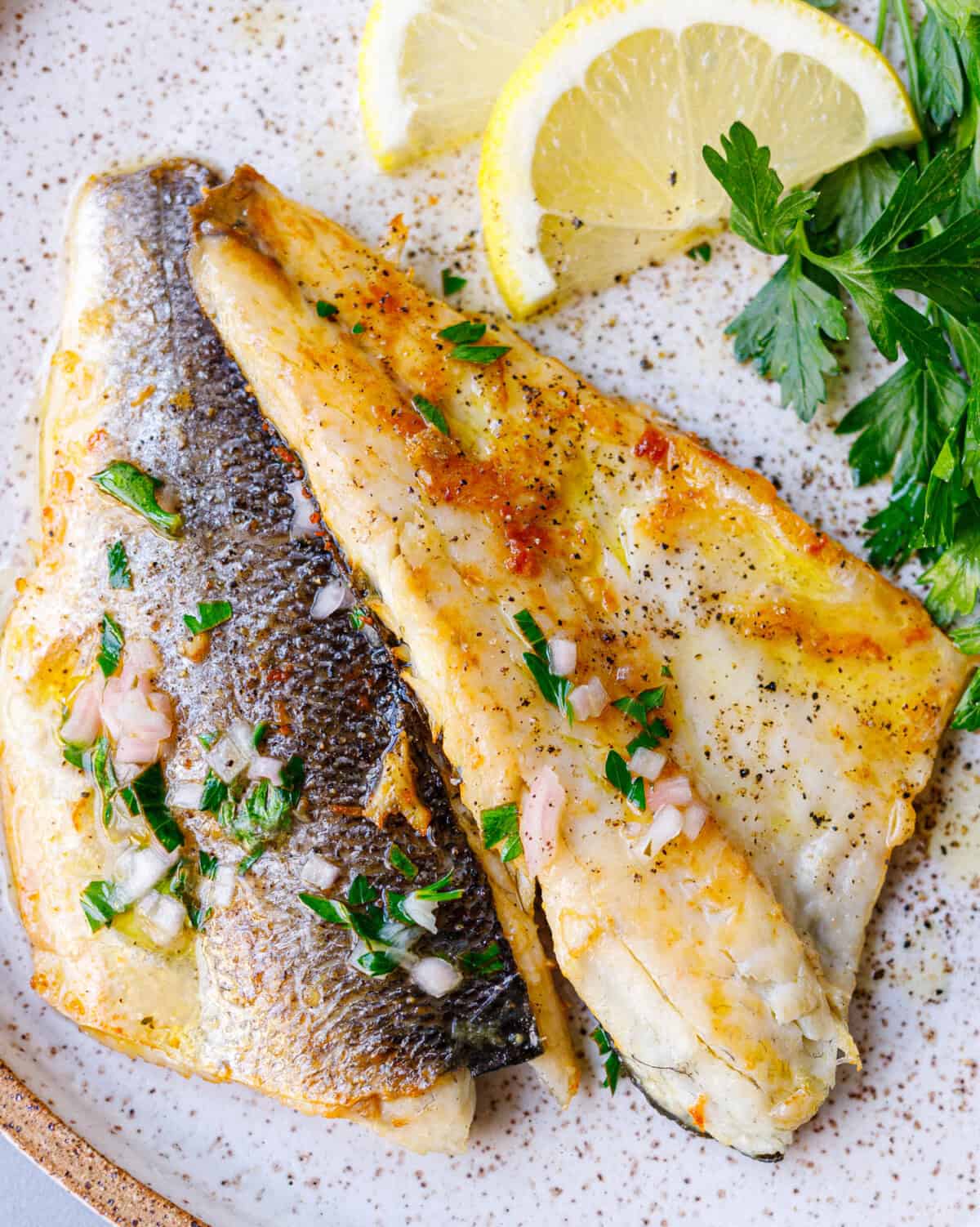 Two plated branzino fillets, one skin-side and one flesh-side up, with lemon and parsley