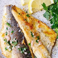Two plated branzino fillets, one skin-side and one flesh-side up, with lemon and parsley