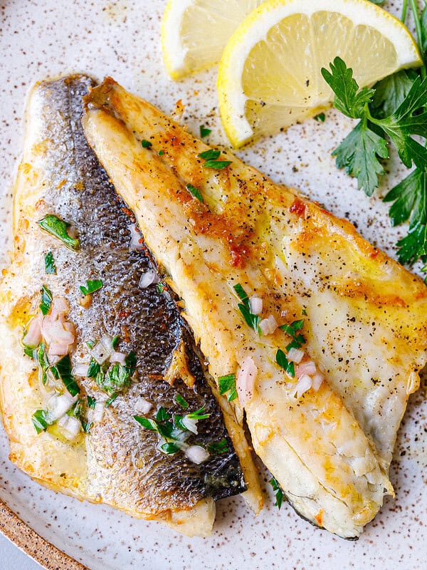 Two plated branzino fillets, one skin-side and one flesh-side up, with lemon and parsley