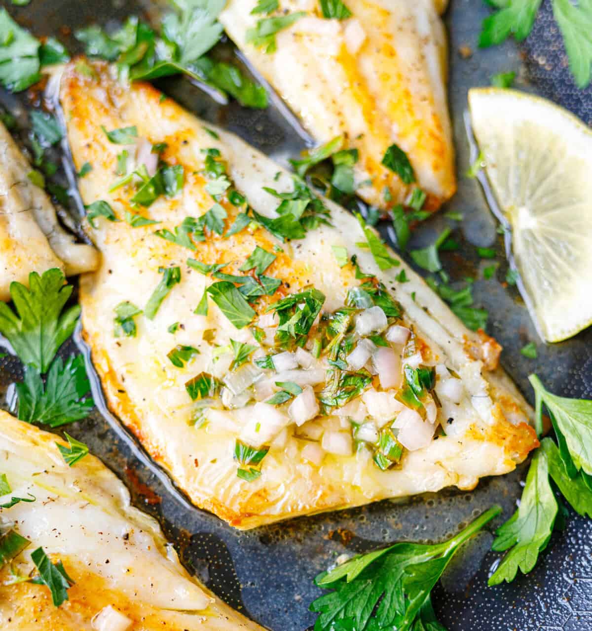 Close-up of a pan-seared branzino fillet topped with shallot, parsley, and lemon butter sauce