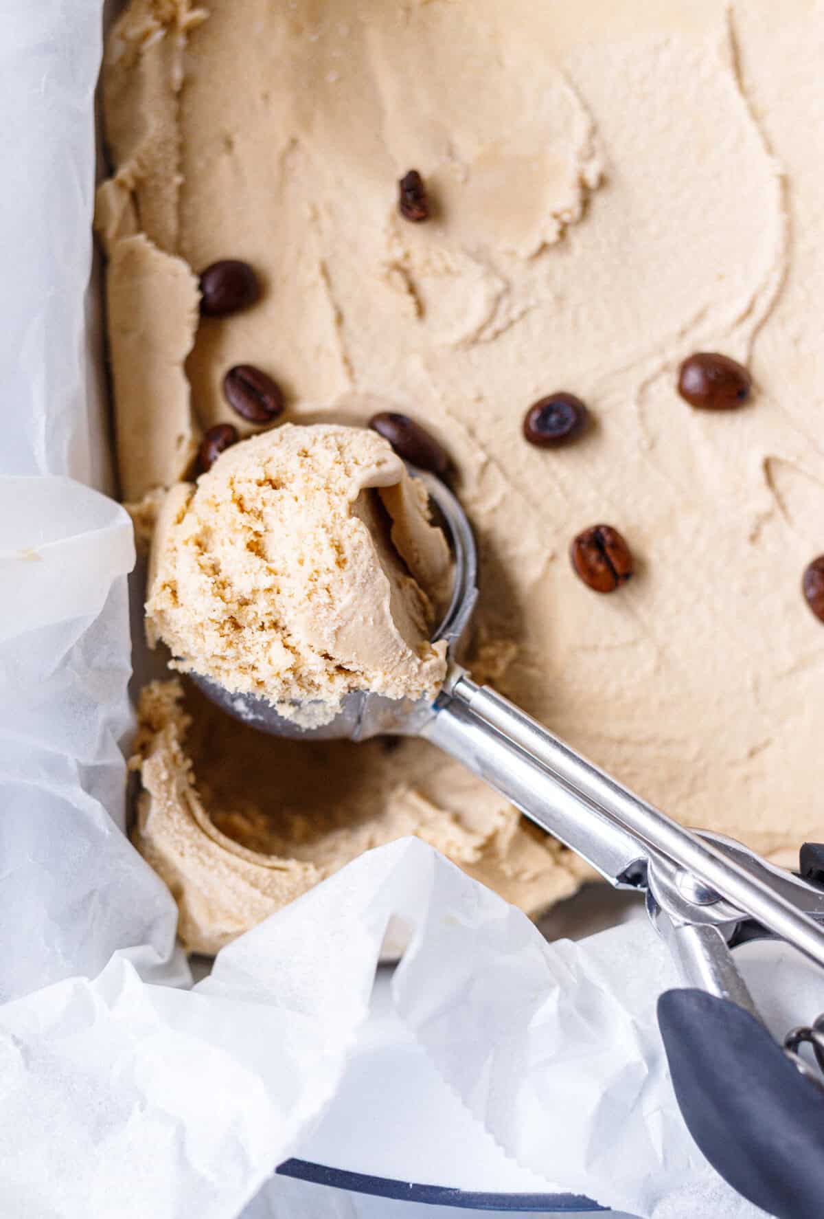 A loaf pan lined with parchment and coffee ice cream inside, scooped with a cookie scoop