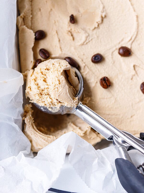 A loaf pan lined with parchment and coffee ice cream inside, scooped with a cookie scoop