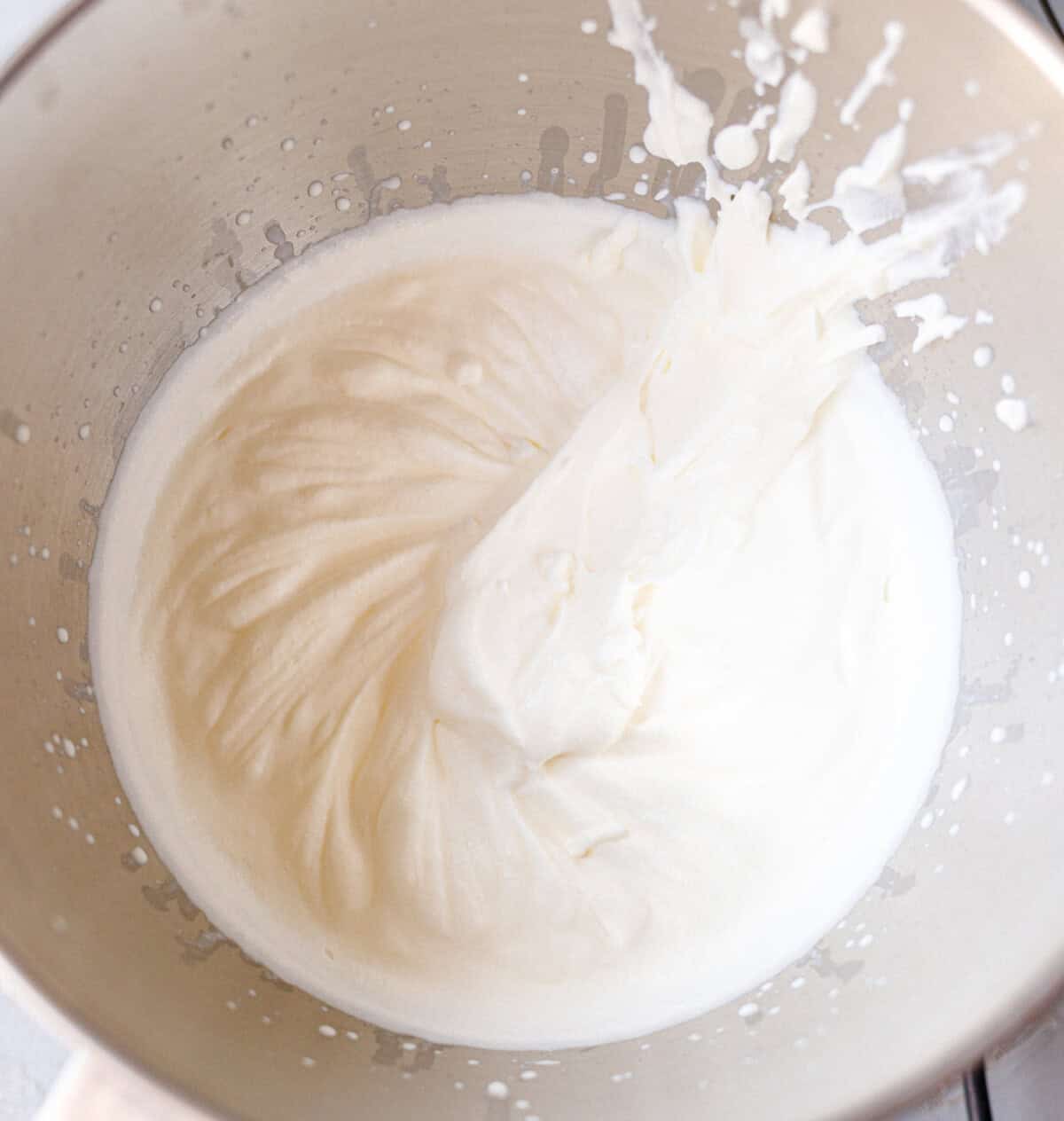 Heavy cream whipped to stiff peaks in a stand mixer bowl for eggless chocolate ice cream