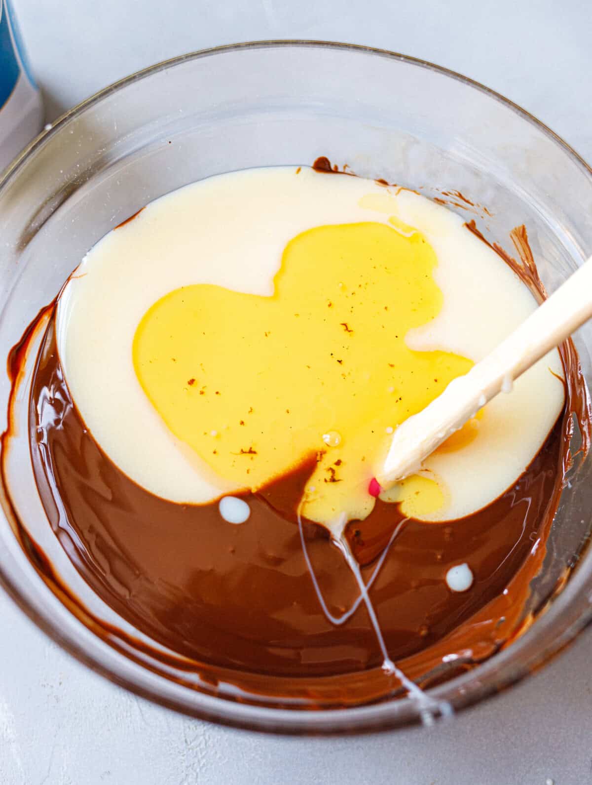 Heavy cream and vanilla added to melted chocolate in a glass bowl