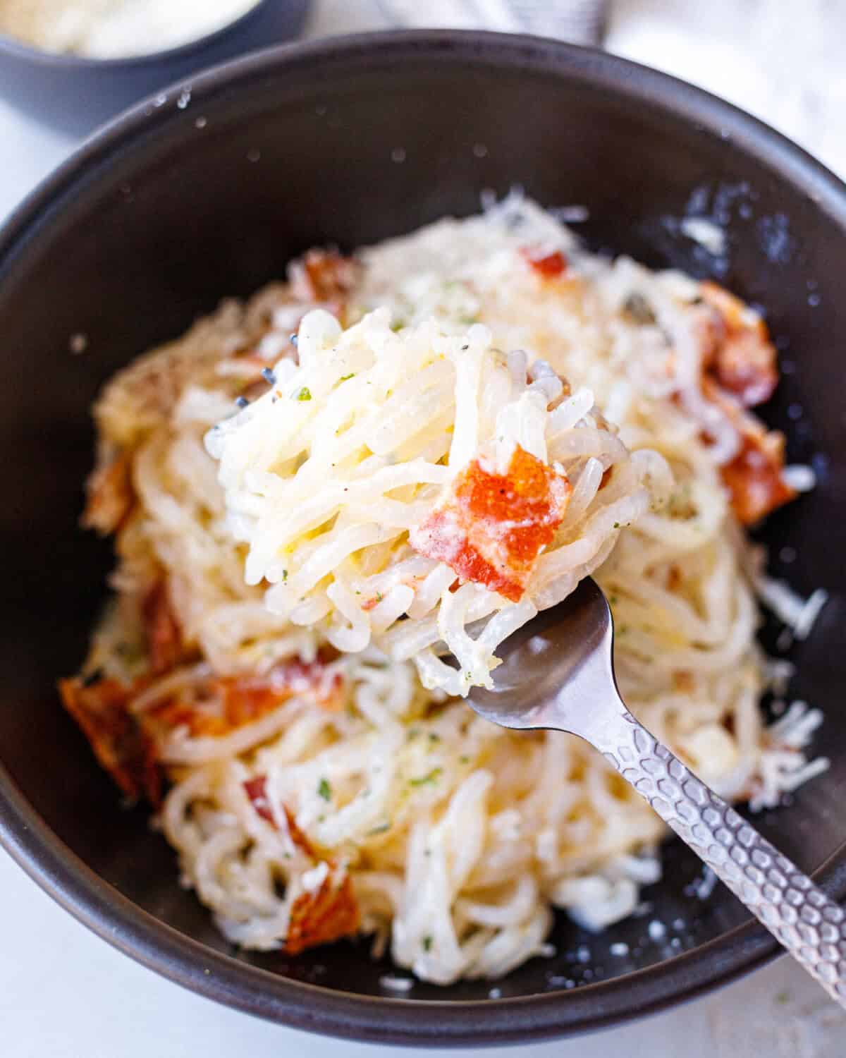 Forkful of creamy konjac carbonara with shirataki noodles, parmesan sauce, and crispy bacon