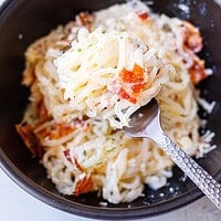 Forkful of creamy konjac carbonara with shirataki noodles, parmesan sauce, and crispy bacon