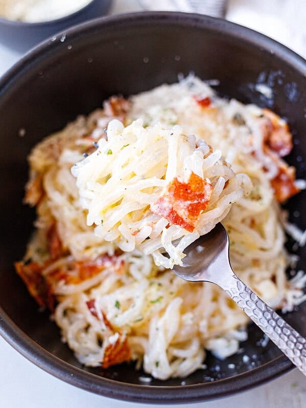 Forkful of creamy konjac carbonara with shirataki noodles, parmesan sauce, and crispy bacon