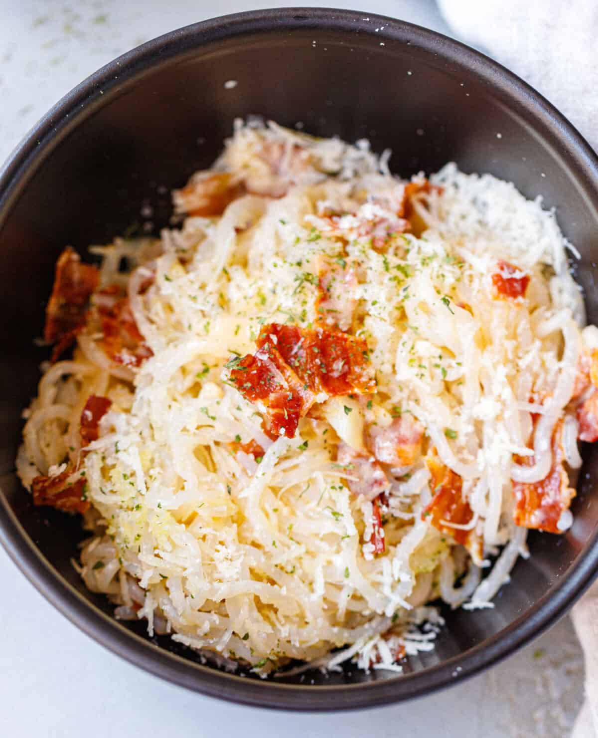 Bowl of konjac carbonara topped with crispy bacon, grated parmesan, and parsley