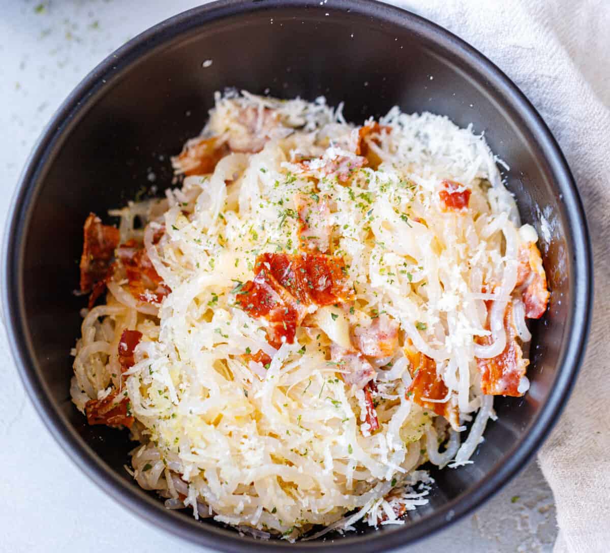 Konjac noodle carbonara in a dark bowl with bacon and freshly grated parmesan on top
