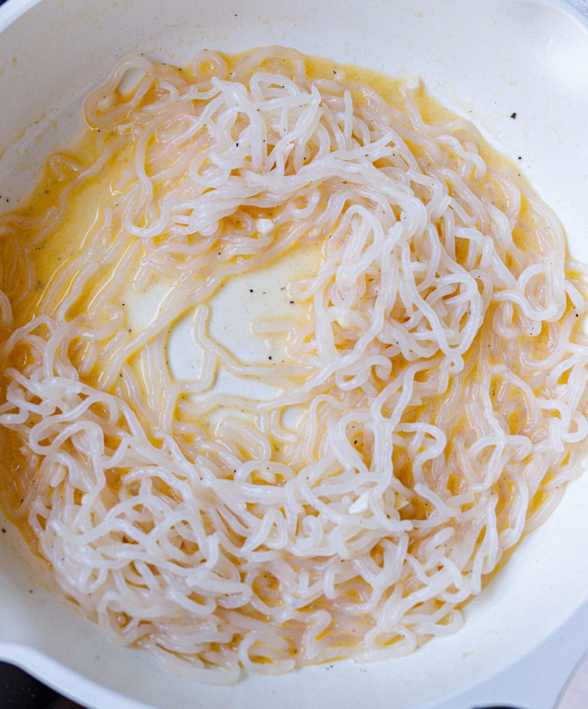 Konjac noodles coated in a creamy egg and parmesan carbonara sauce in a white pan