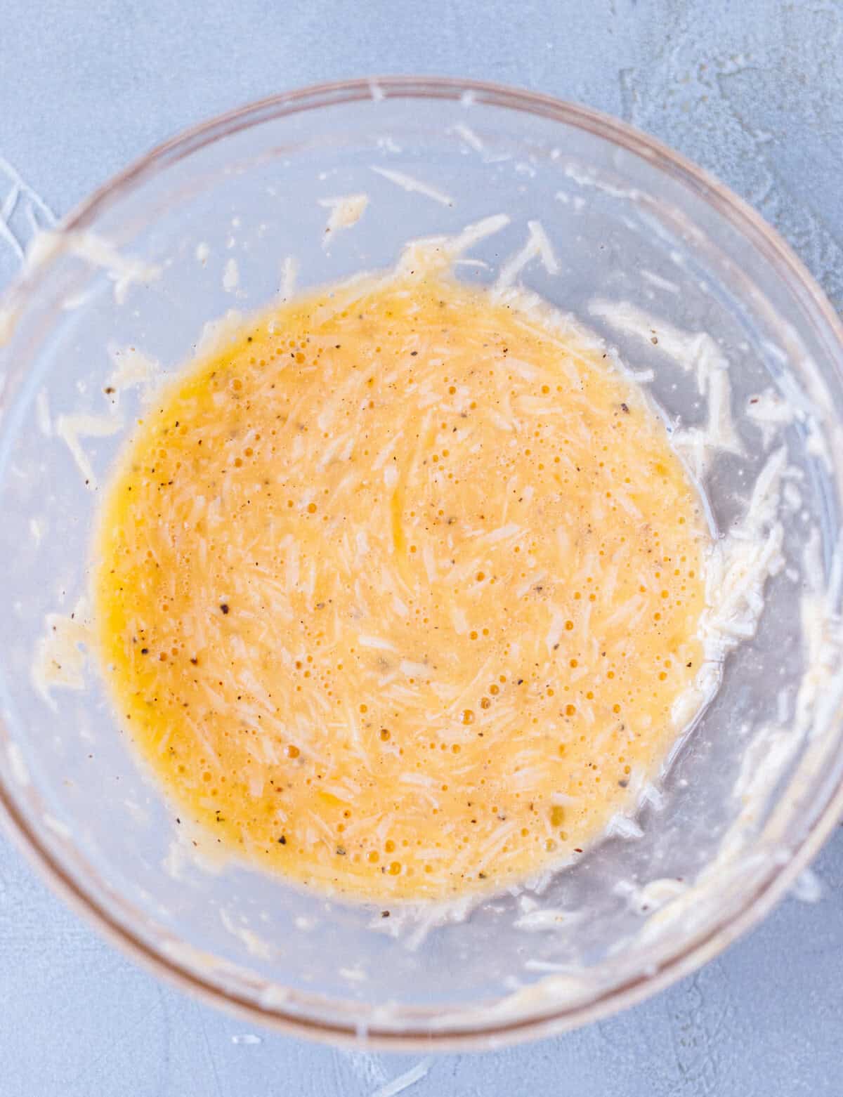Whisked egg, cream, and grated parmesan in a glass bowl for konjac carbonara sauce