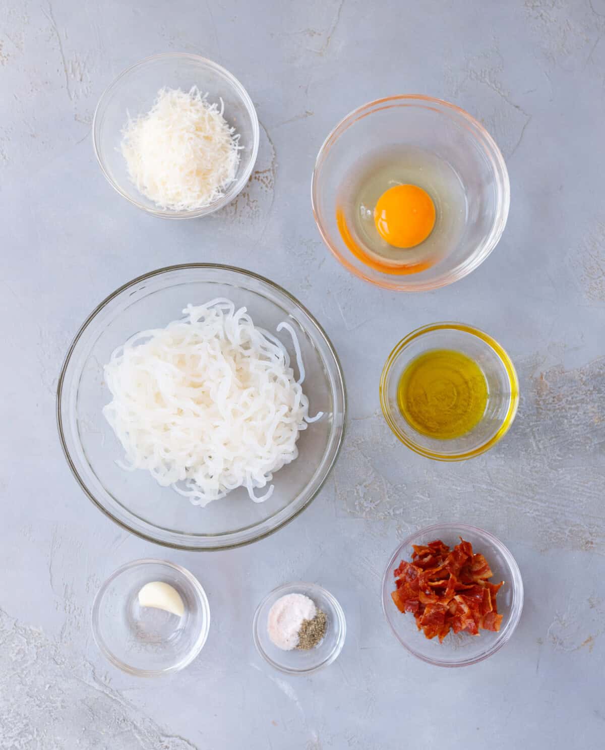 Ingredients for konjac carbonara — shirataki noodles, egg, parmesan, olive oil, garlic, bacon, salt, and pepper