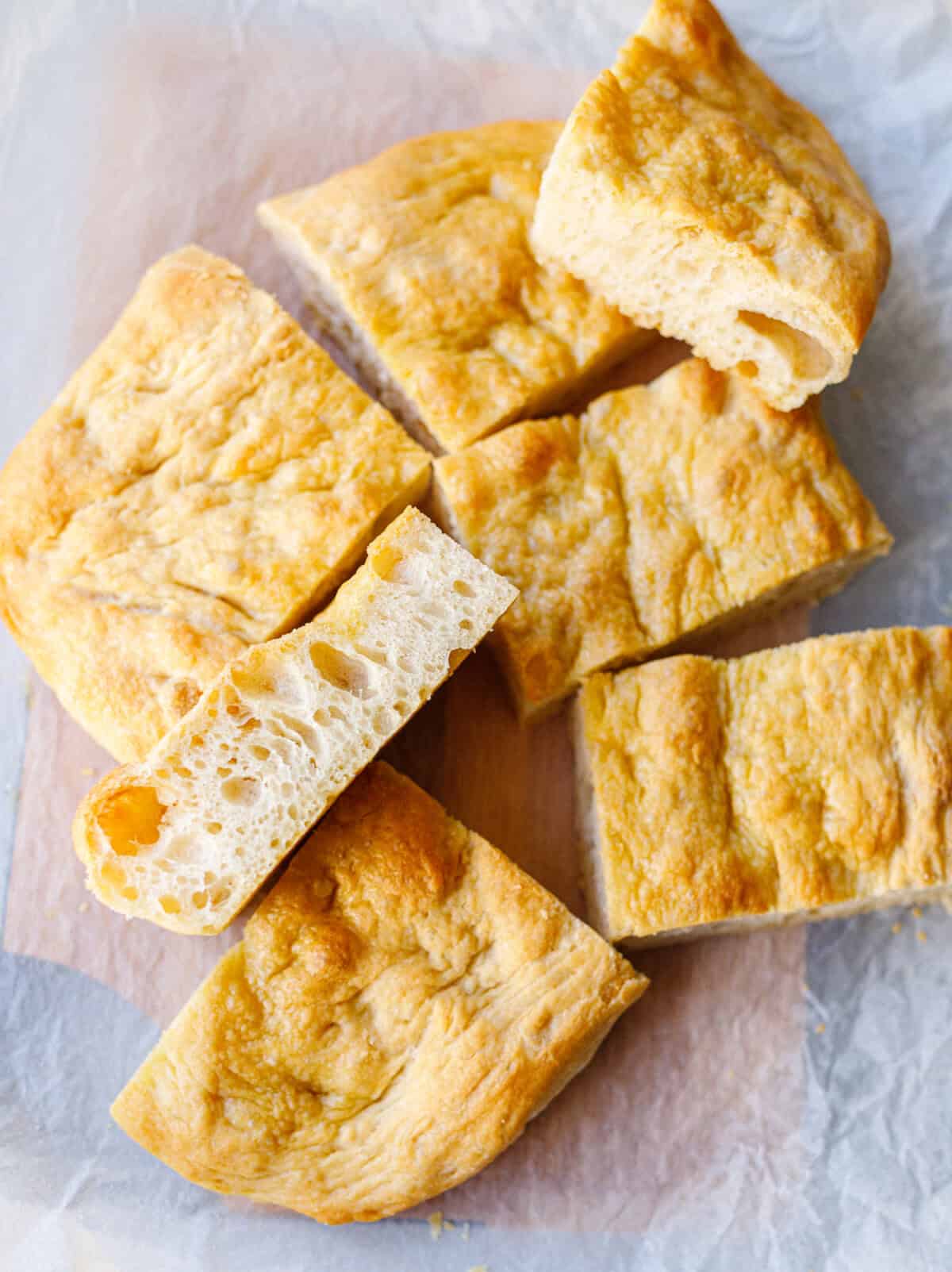 Sliced homemade focaccia on parchment with one piece turned to show the airy crumb
