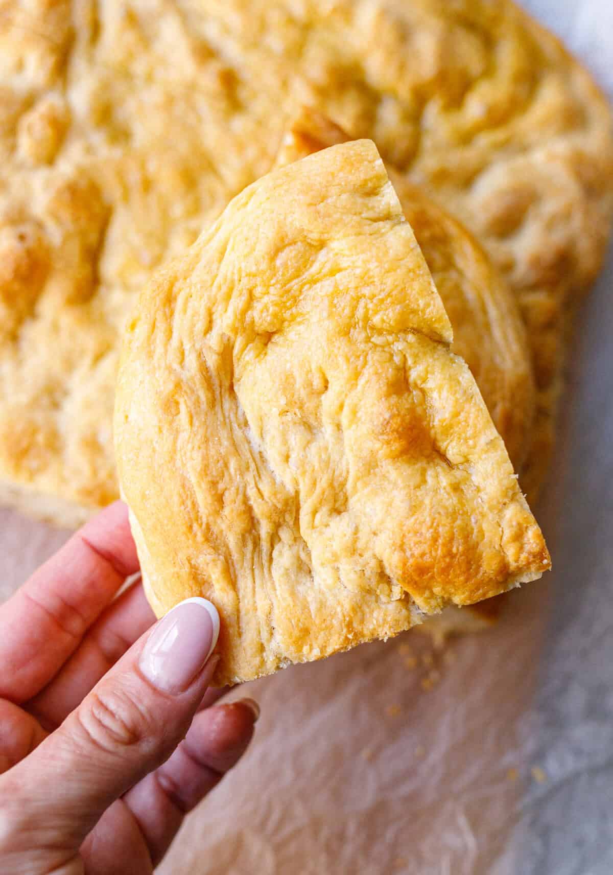 Hand holding a piece of golden homemade focaccia with a crackly olive-oil top
