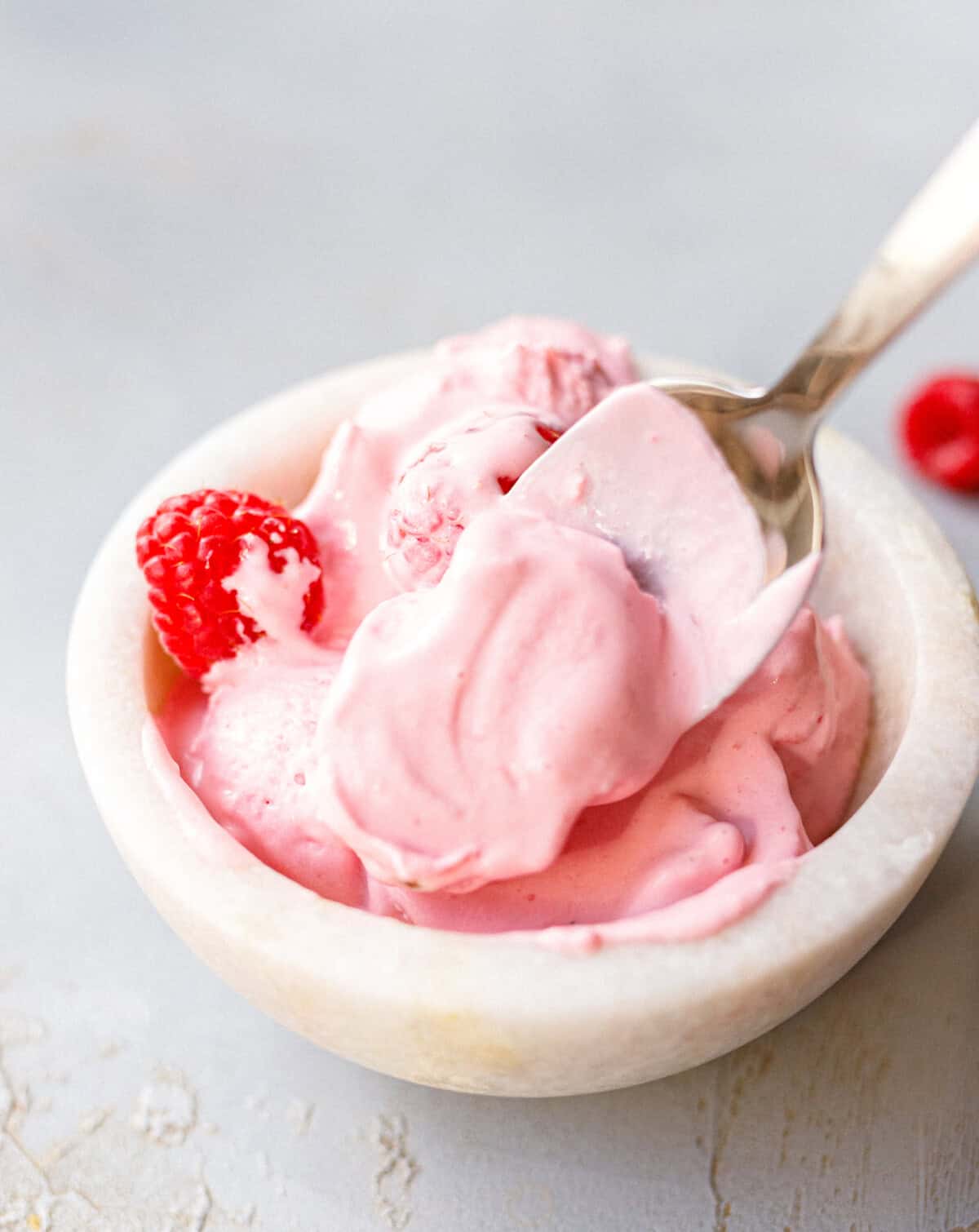 Spoonful of creamy raspberry mascarpone ice cream lifted from a marble bowl