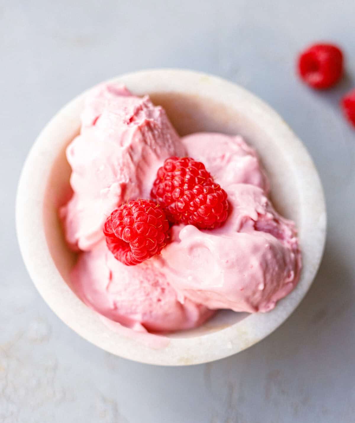 Bowl of low-carb raspberry mascarpone ice cream topped with two fresh raspberries