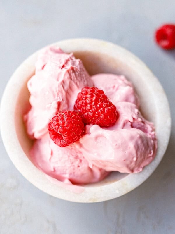 Bowl of low-carb raspberry mascarpone ice cream topped with two fresh raspberries