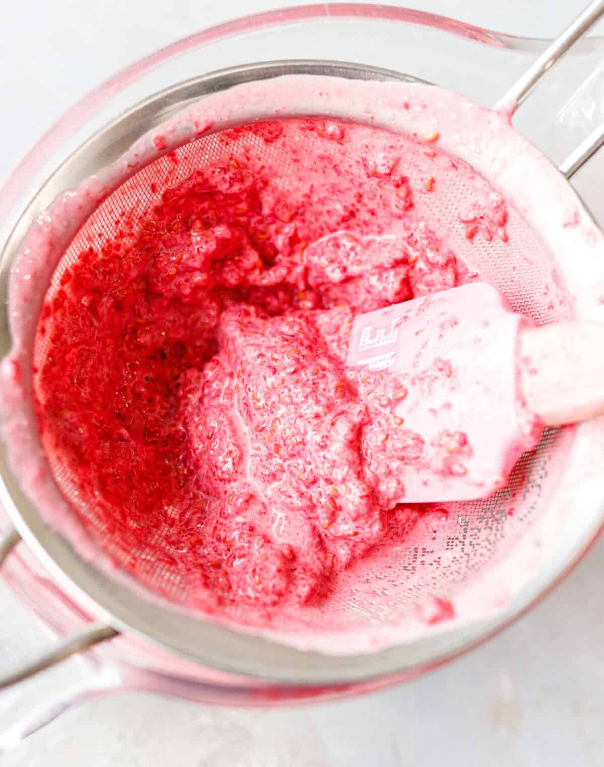 Straining raspberry seeds from the blended base through a mesh sieve for smooth mascarpone ice cream