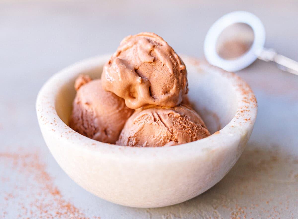 Three scoops of no-churn chocolate ice cream in a marble bowl dusted with cocoa
