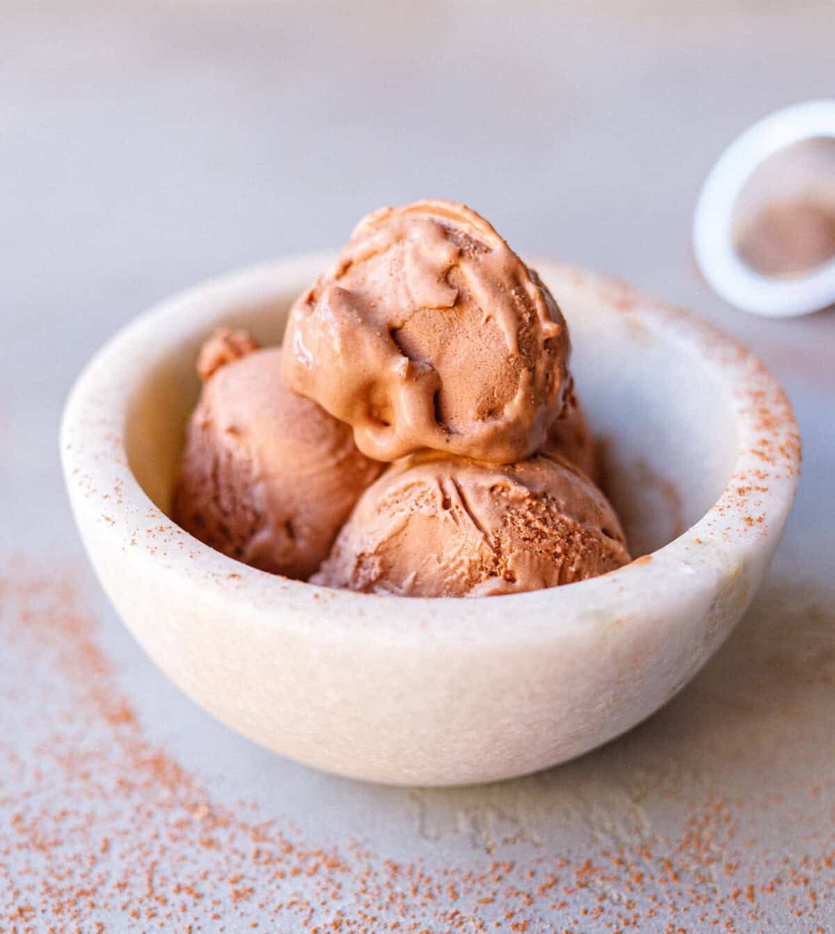 Three scoops of no-churn chocolate ice cream in a marble bowl dusted with cocoa