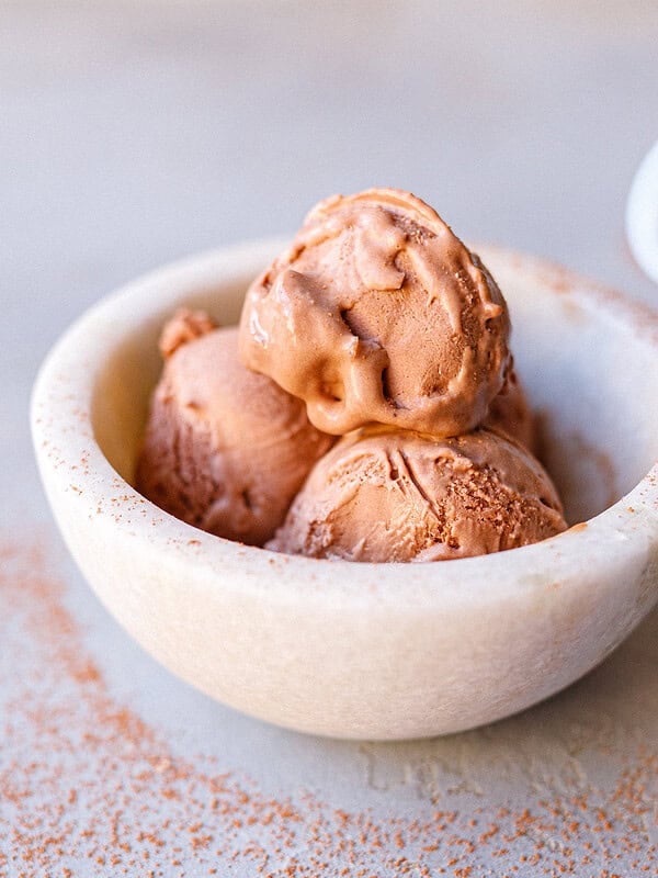 Three scoops of no-churn chocolate ice cream in a marble bowl dusted with cocoa