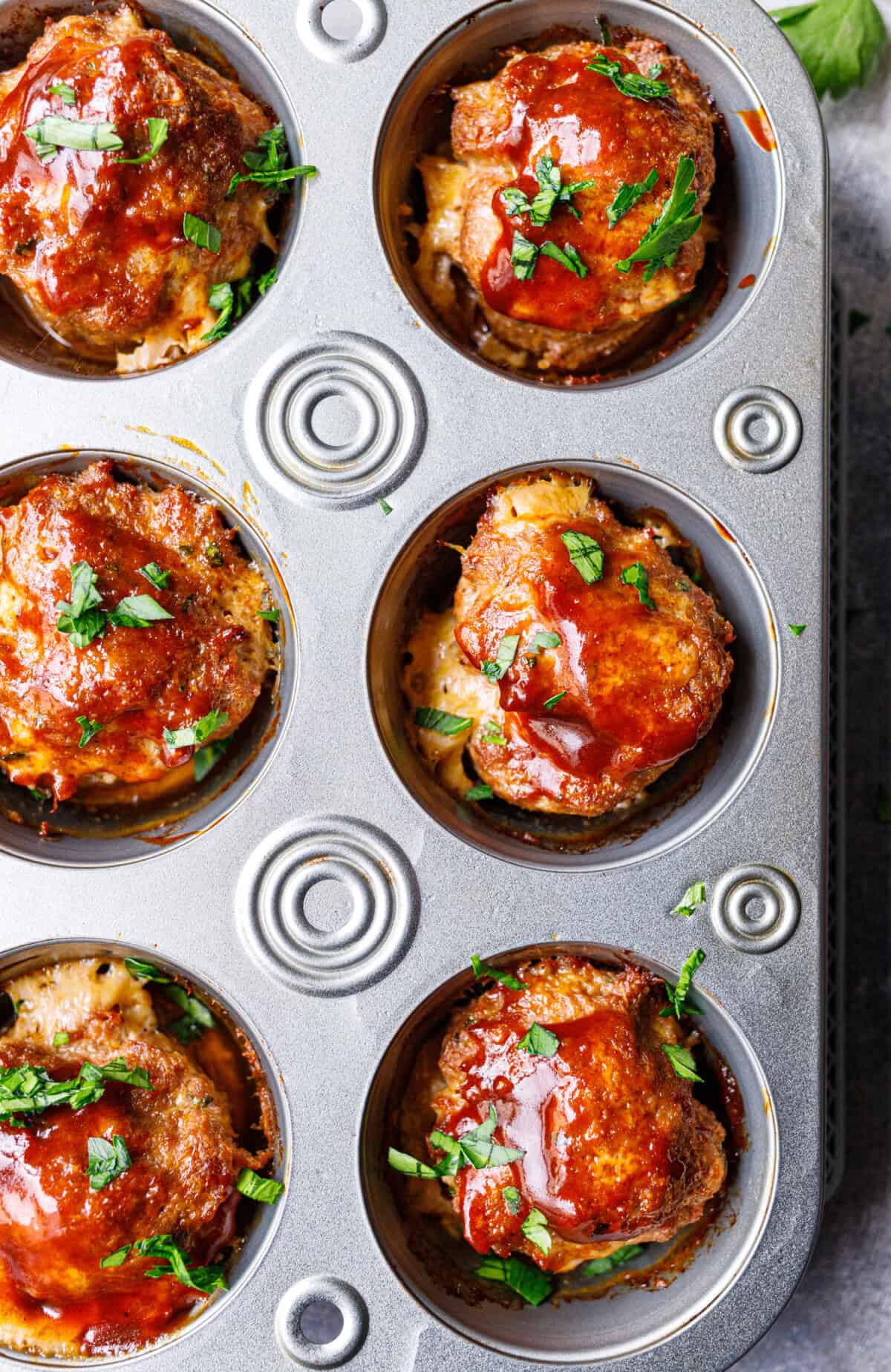 BBQ-glazed mini meatloaf muffins topped with parsley in a metal muffin tin