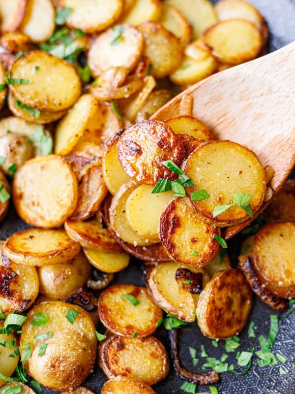 Wooden spoon lifting crispy fried potatoes and onions from the pan with parsley