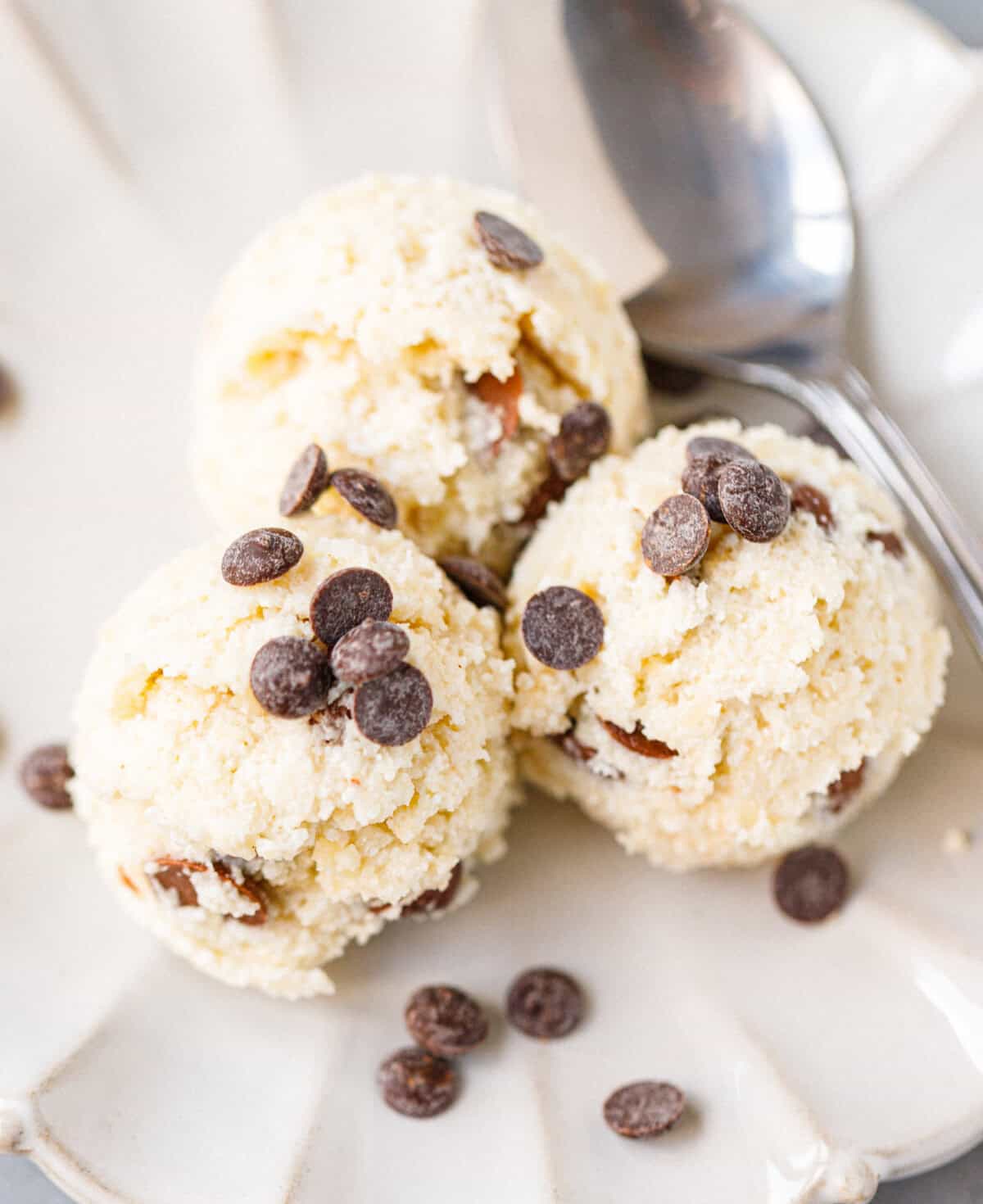 Three scoops of cottage cheese cookie dough topped with chocolate chips on a scalloped plate