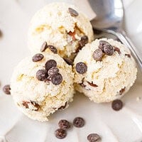 Three scoops of cottage cheese cookie dough topped with chocolate chips on a scalloped plate
