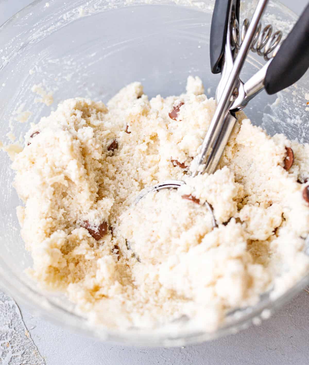 Cottage cheese cookie dough in a glass bowl with a cookie scoop and chocolate chips mixed in