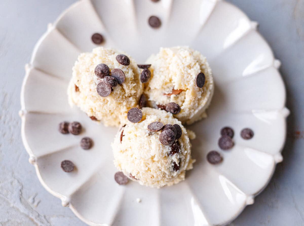 Three balls of low-carb protein cookie dough on a white scalloped plate with chocolate chips