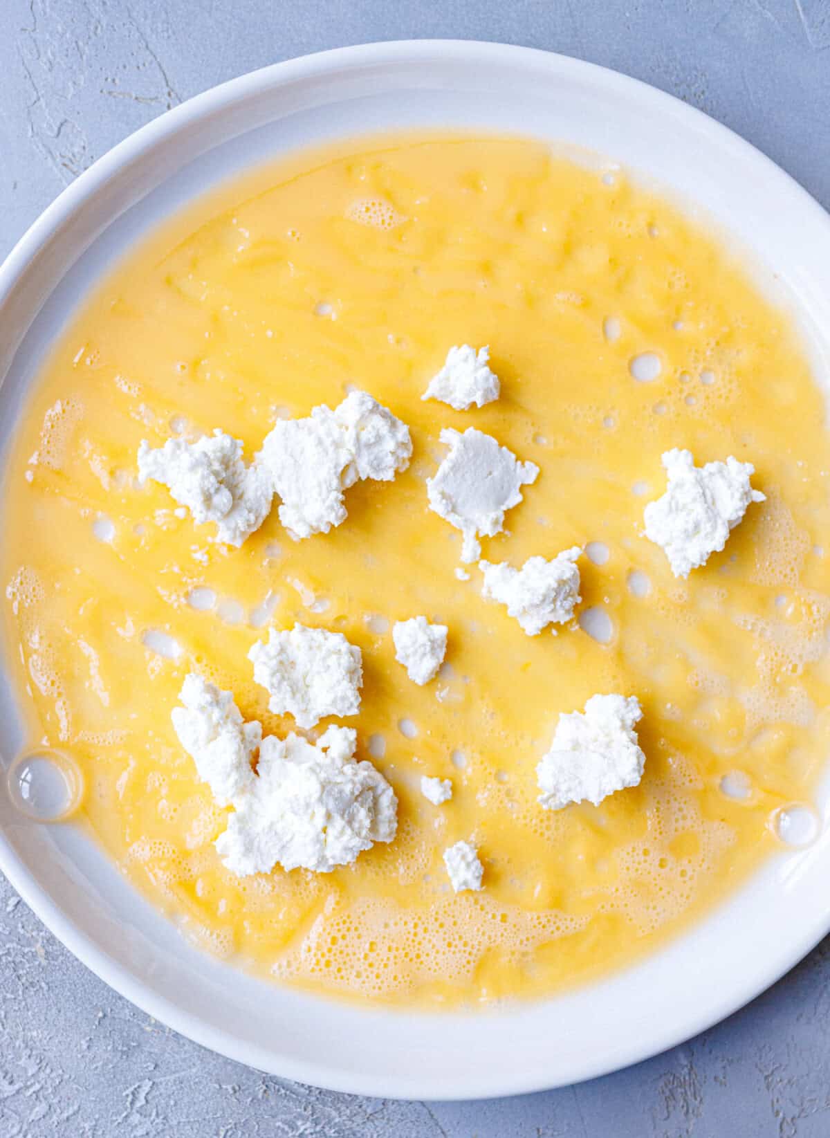 Crumbled white cheese scattered over egg wash in a white dish