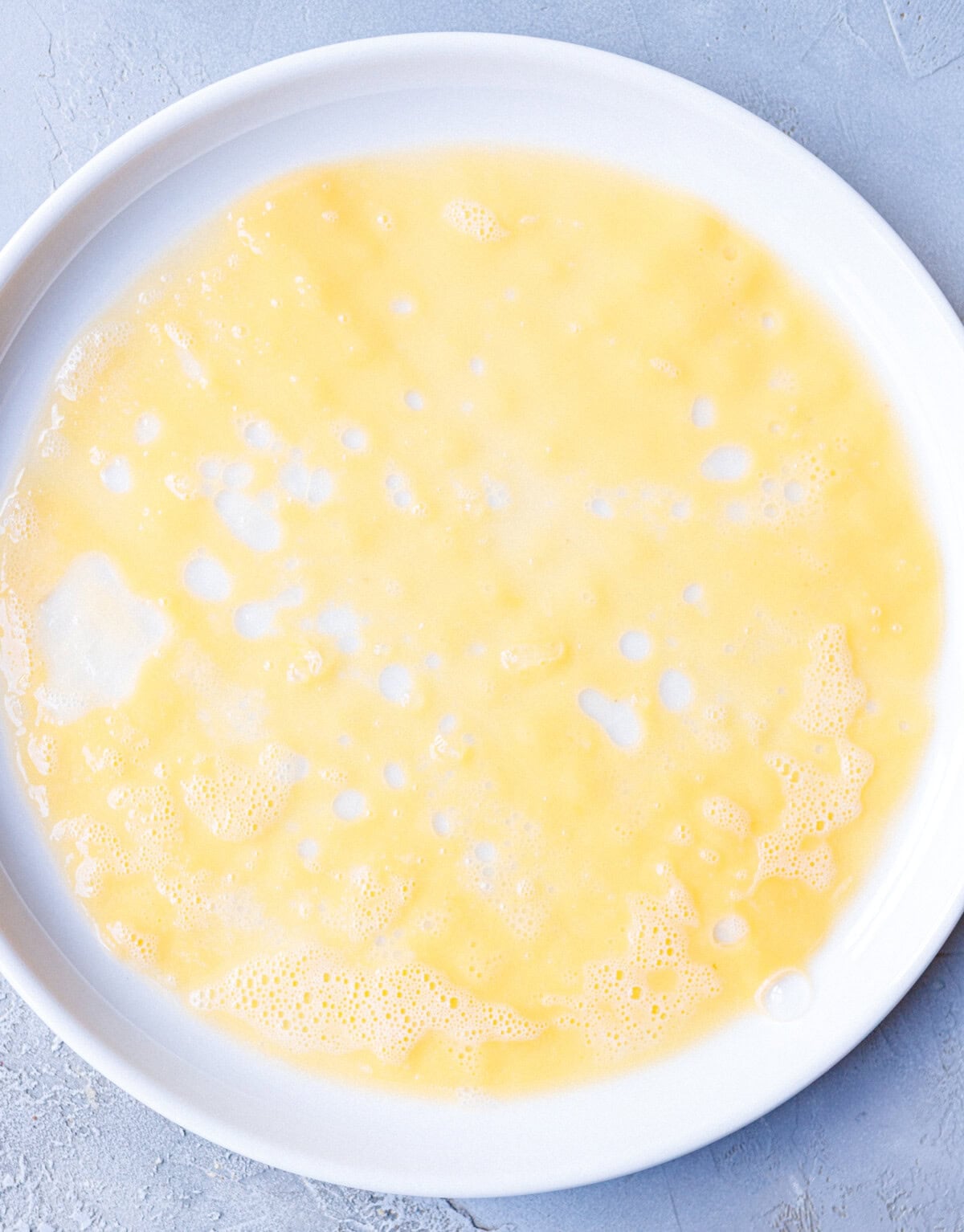 Egg mixture whisked with milk in a wide dish, ready for dipping rice paper sheets