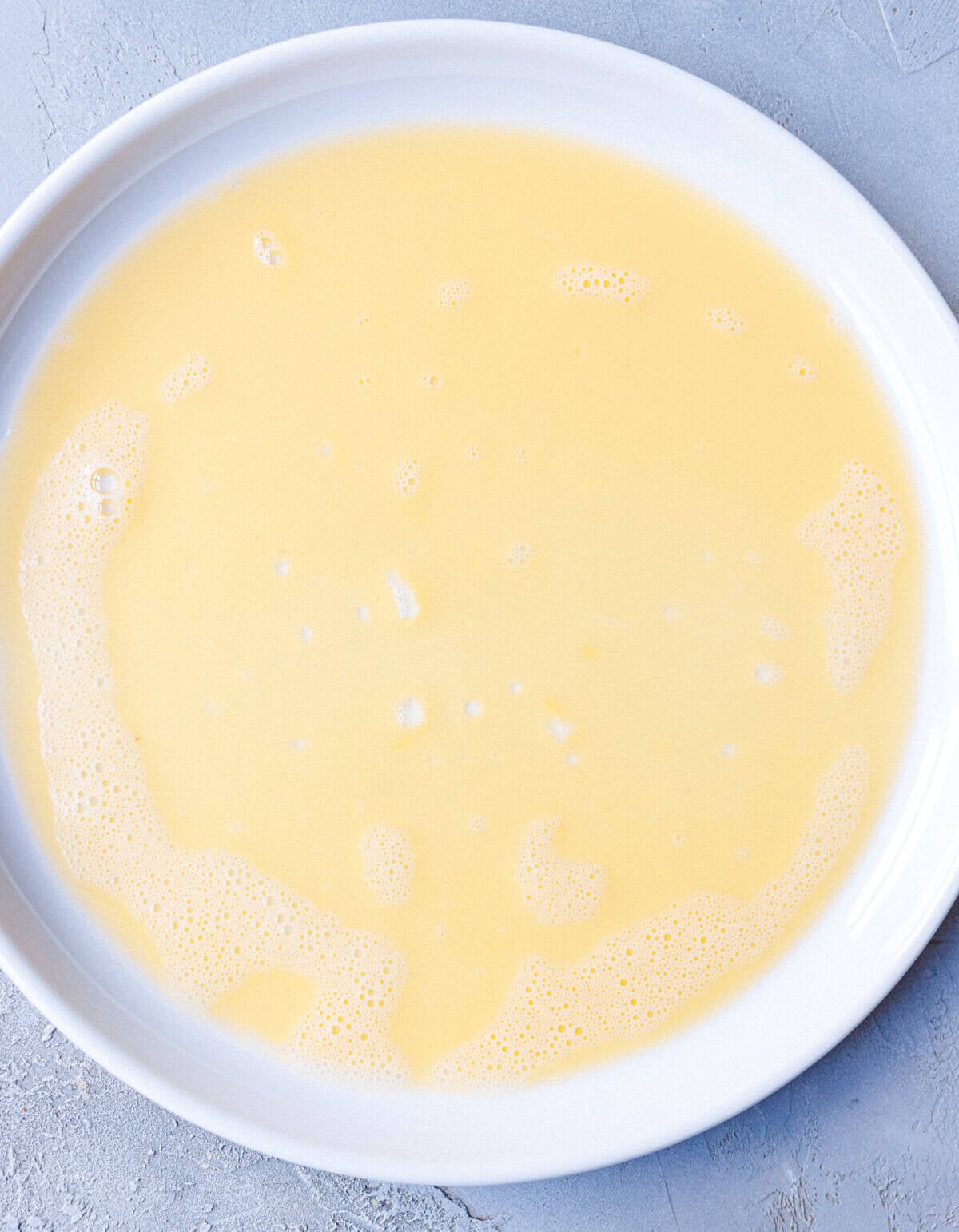 Beaten egg and milk mixture in a shallow white dish for dipping rice paper