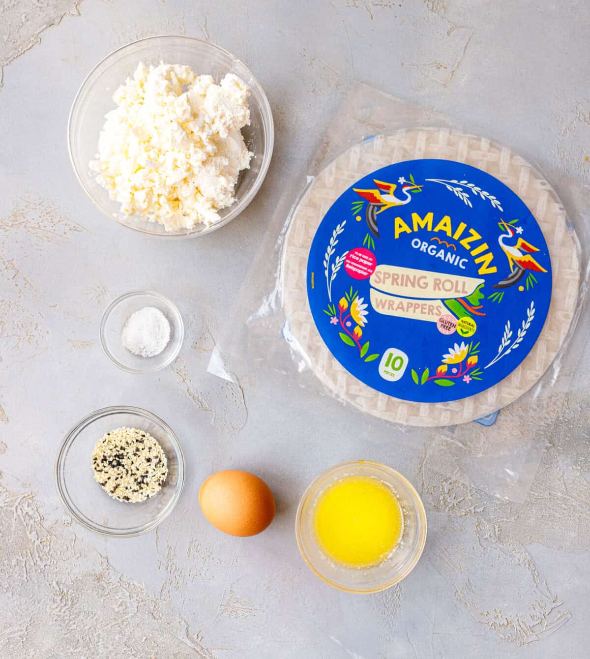 Ingredients for rice paper banitsa — crumbled feta, rice paper wrappers, sesame seeds, an egg, melted butter, and salt
