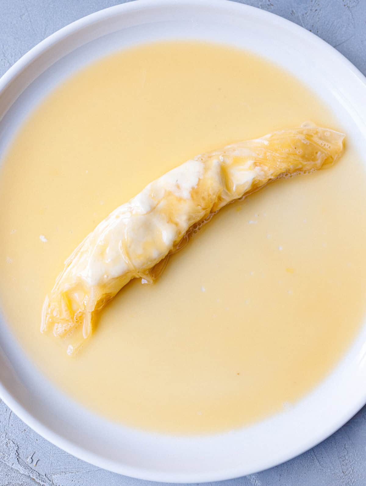 A single rolled rice paper banitsa resting in egg wash before air frying