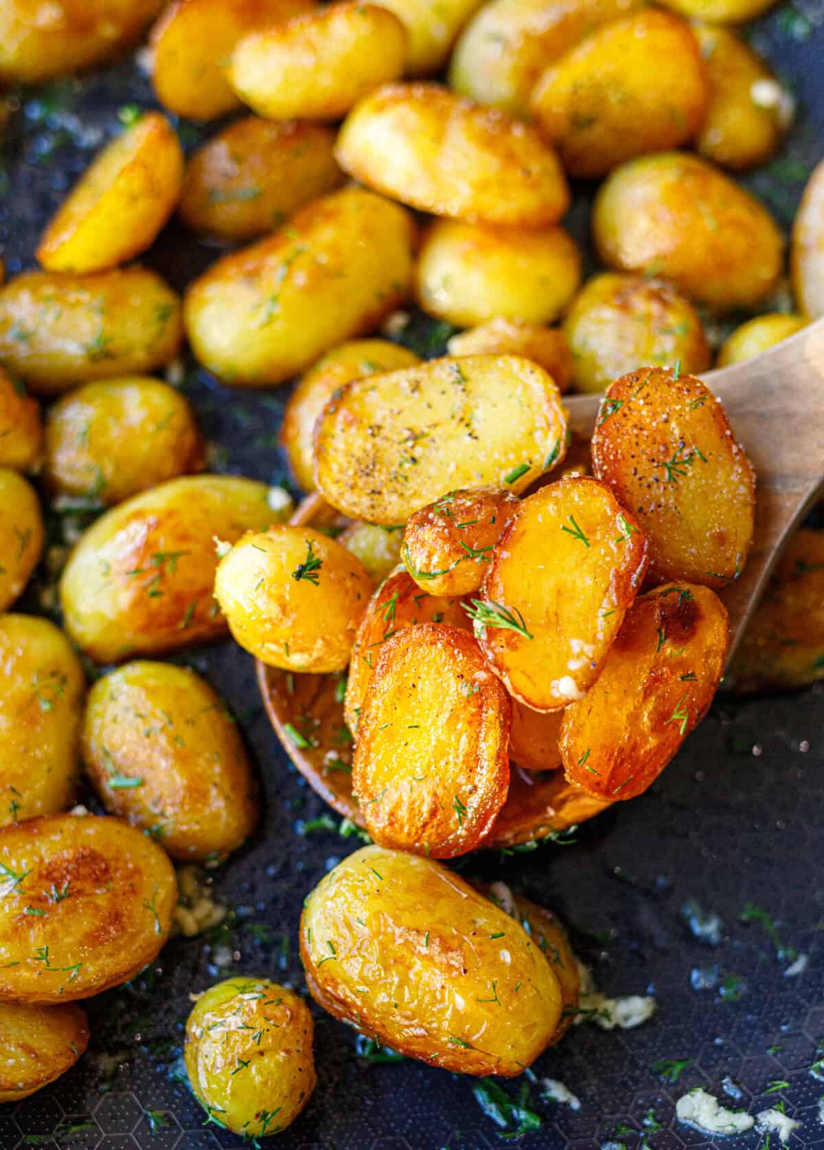 Wooden spoon lifting crispy sautéed potatoes with dill from the pan