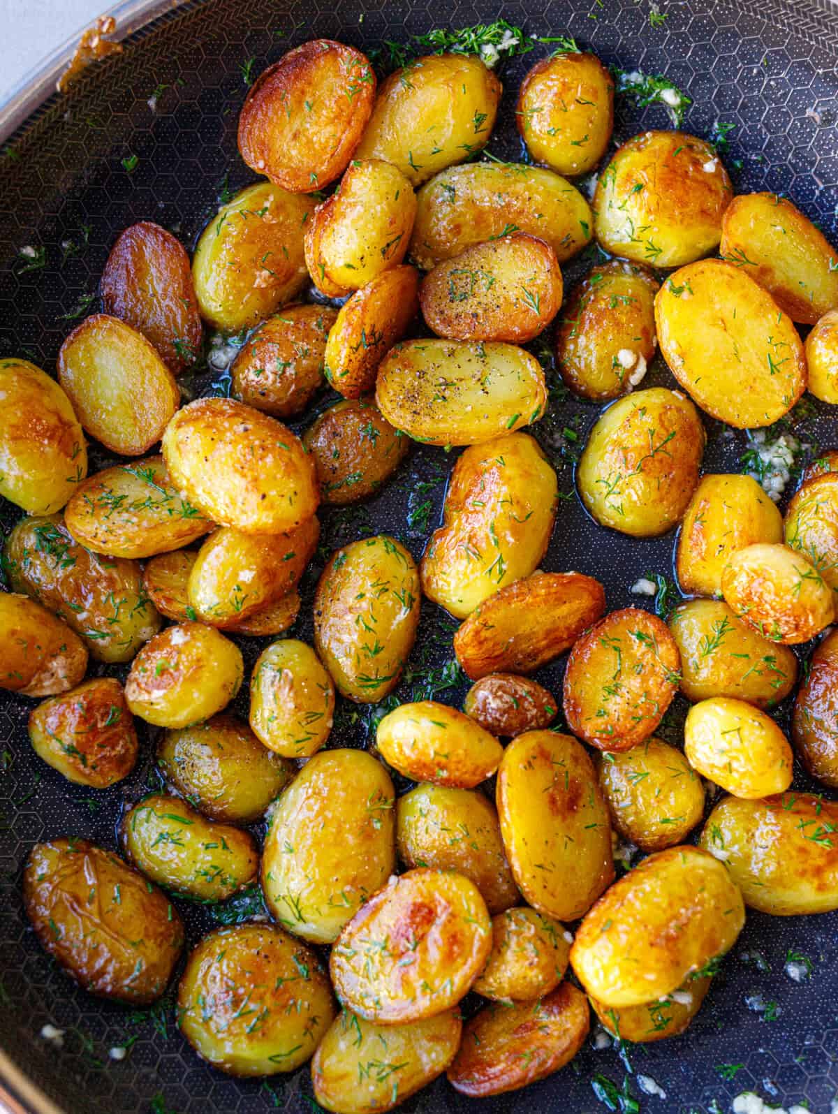 Close-up of golden Bulgarian sautéed potatoes with dill and garlic in a skillet