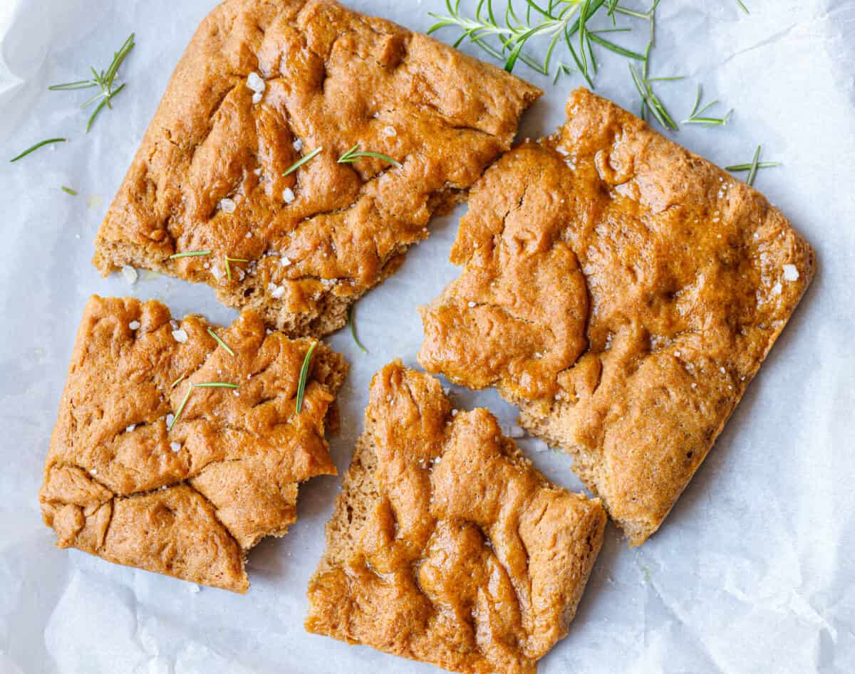 Whole spelt focaccia cut into squares on parchment with rosemary and flaky salt
