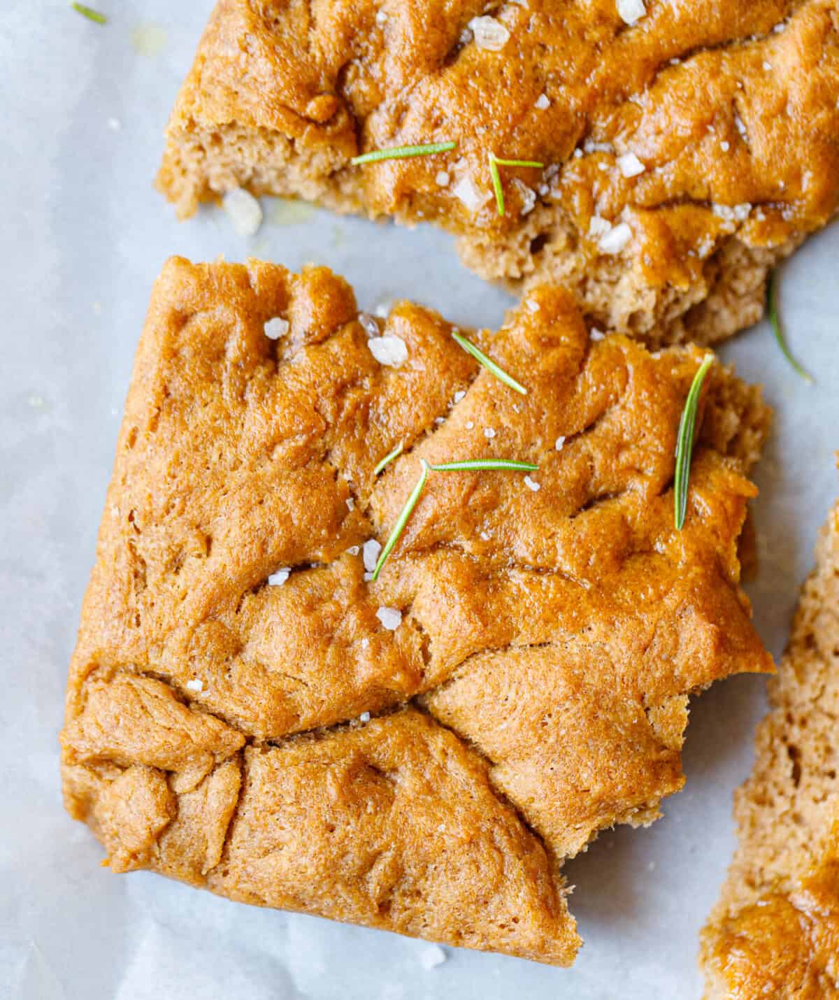 Close-up of spelt flour focaccia squares topped with rosemary sprigs and sea salt
