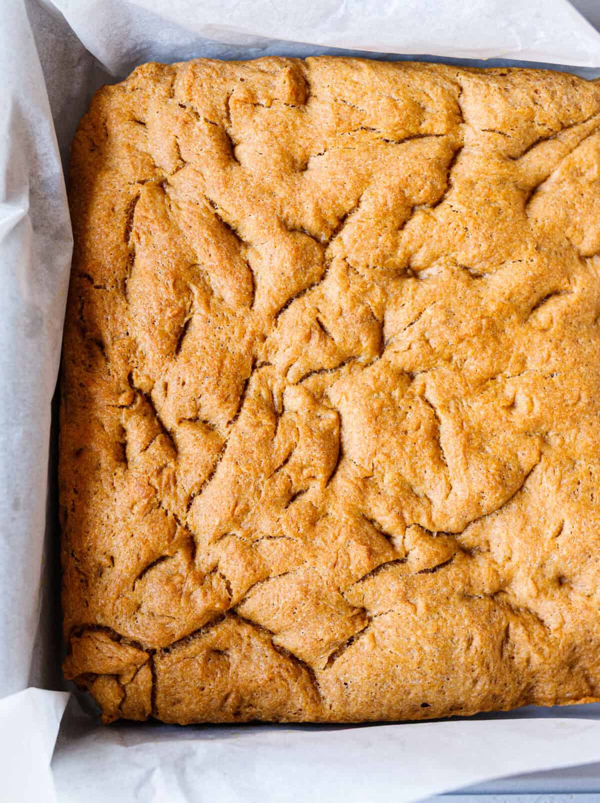 Baked homemade focaccia in a parchment-lined square pan, golden and dimpled