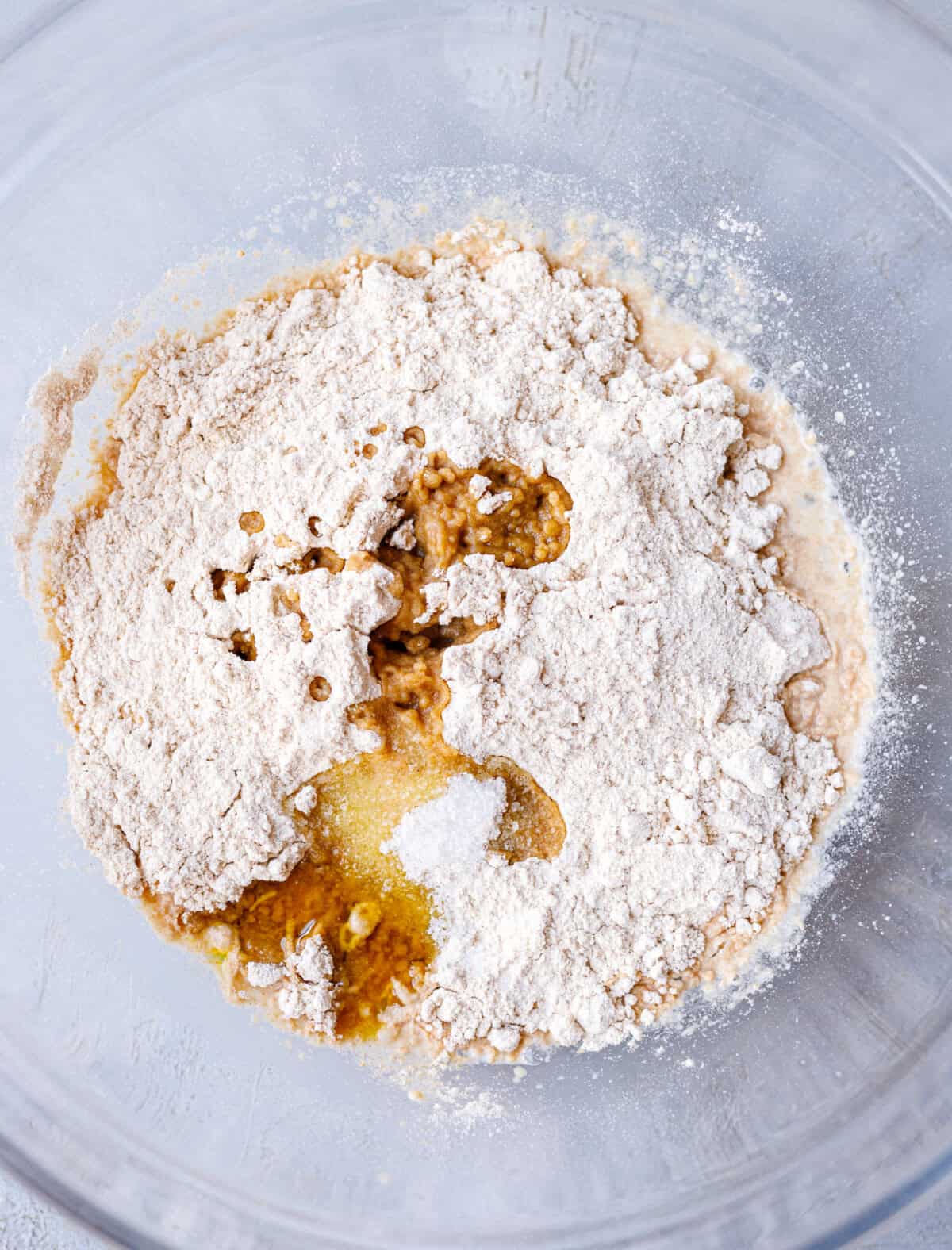 Spelt flour, salt and olive oil added to bubbly yeast mixture in a glass bowl