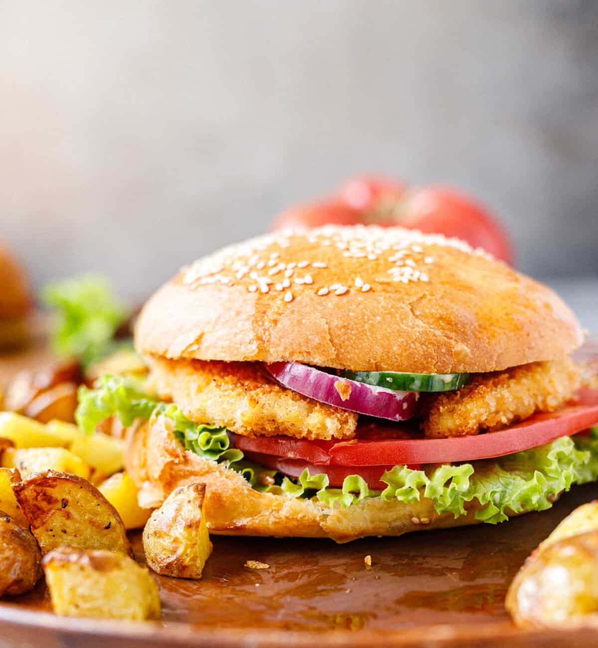 Assembled crispy chicken burger with lettuce, tomato, onion, and cucumber on a sesame bun